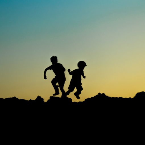 contraluz de dos niños corriendo sobre unas rocas