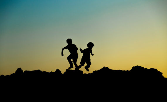 contraluz de dos niños corriendo sobre unas rocas